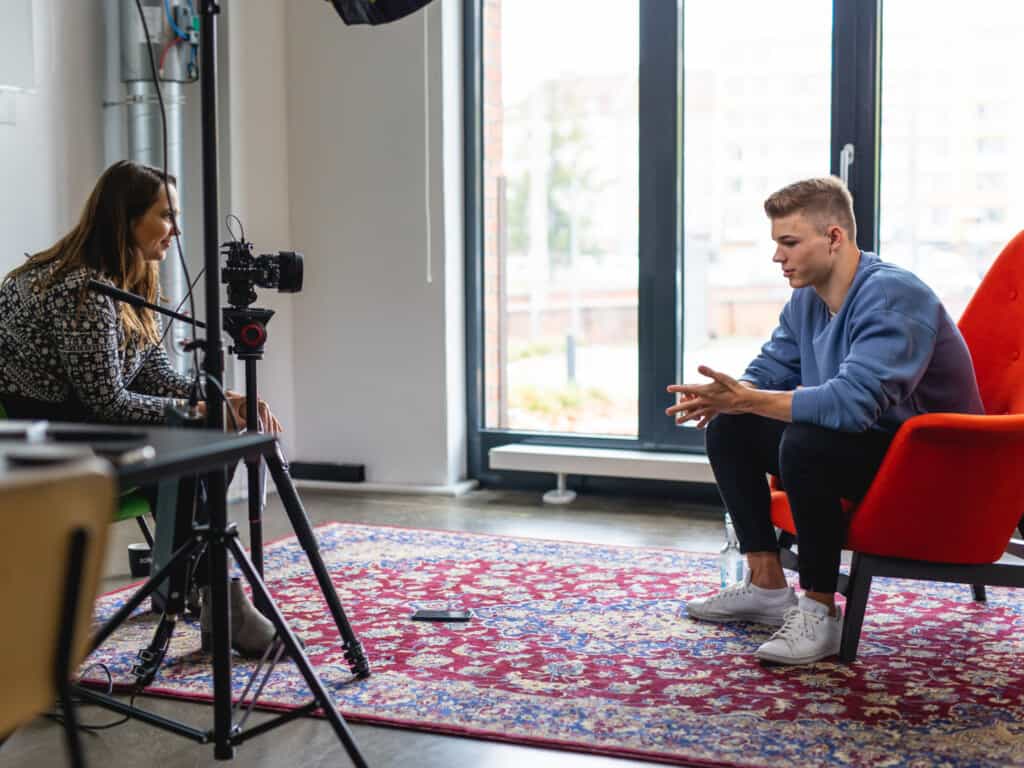 Interviewsituation mit Taliso Engel. Links steht eine Kamera und die Interviewerin, rechts sitzt Taliso auf einem roten Sessel.