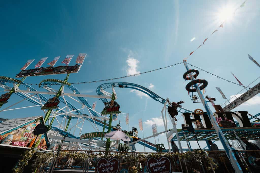Übersicht über eine große Achterbahn mit bunten Schildern und Figuren beim Nürnberger Herbstvolksfest, im Sonnenlicht.