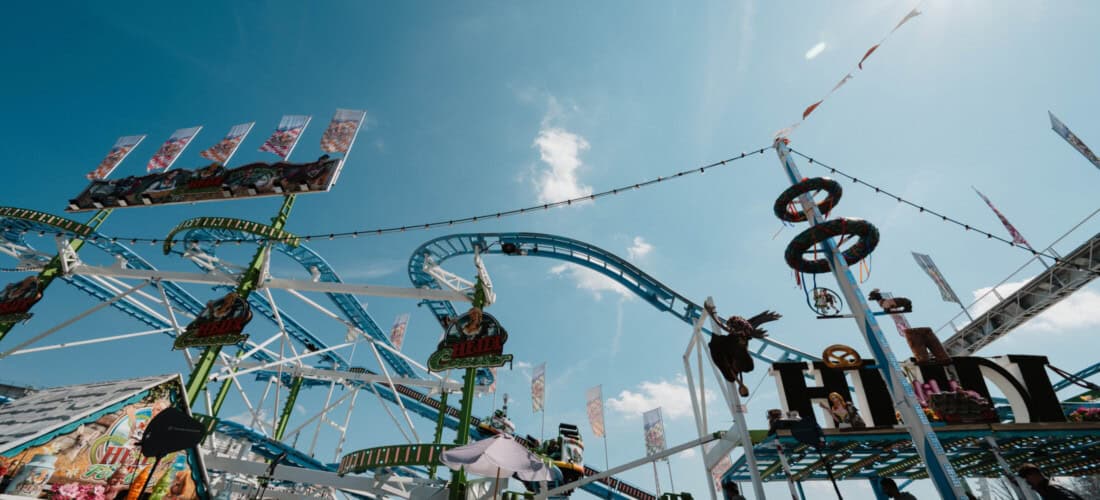 Übersicht über eine große Achterbahn mit bunten Schildern und Figuren beim Nürnberger Herbstvolksfest, im Sonnenlicht.