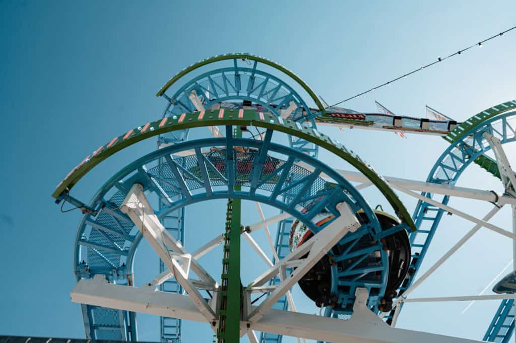 Blick von unten auf eine bunte Achterbahn mit Loopings auf dem Nürnberger Volksfest vor blauem Himmel