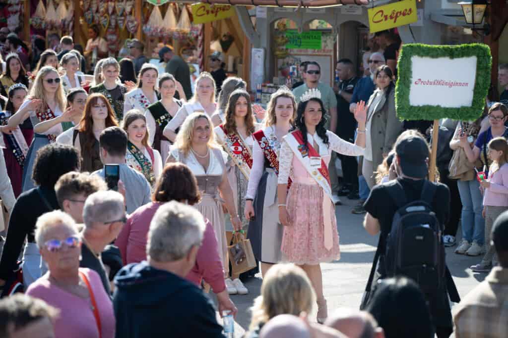 Gruppe von Produkthoheiten in festlicher Tracht und Schärpen beim Umzug auf dem Volksfestgelände.