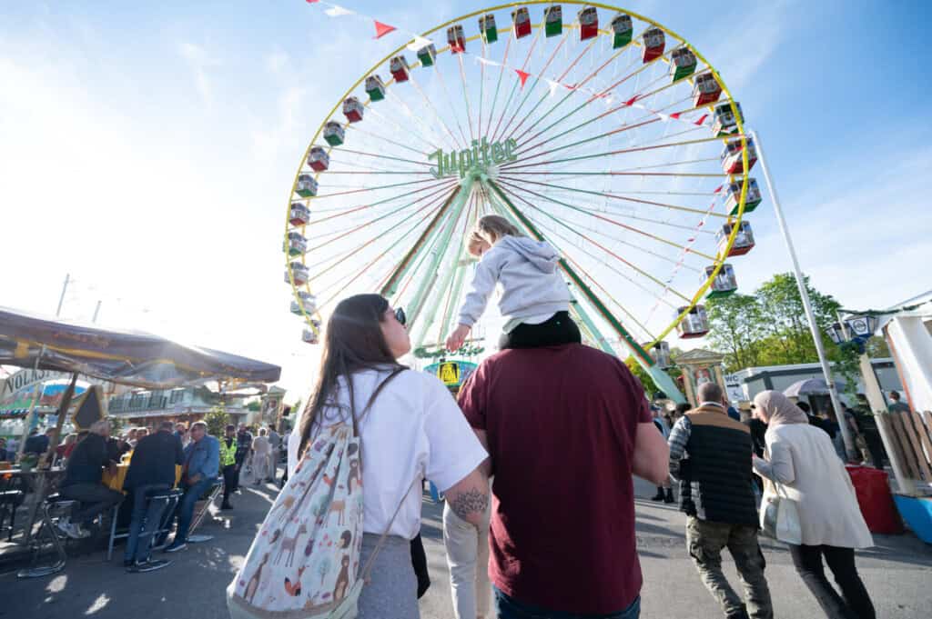 Familie mit Kind auf den Schultern vor dem großen Riesenrad „Jupiter“ auf dem Nürnberger Volksfest.